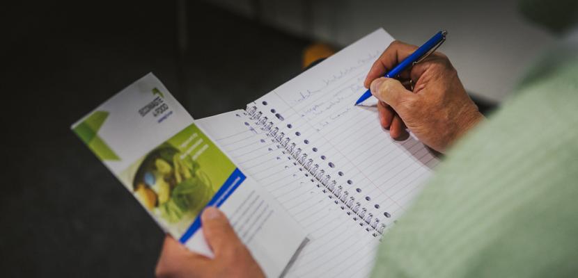 Person writing on a notebook holding a Interreg Europe brochure 