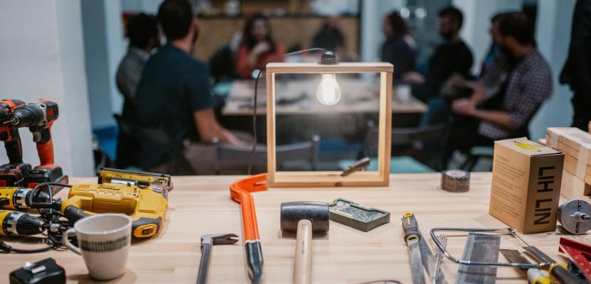 The Library of Things & Repair Café Τhe picture shows a bench with tools and behind it a group of people repairing things