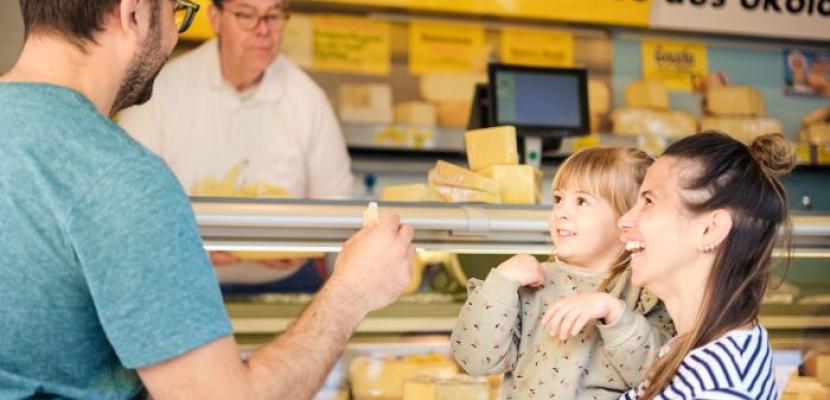 A family buys regional products from a cheese counter at a weekly market.