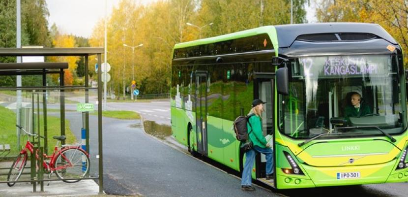 Green electric bus stopped on a bus stop and girl getting on the bus.