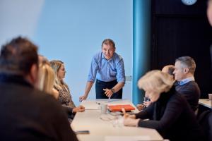Man at end of a table speaking to a group of people Man at end of a table speaking to a group of people