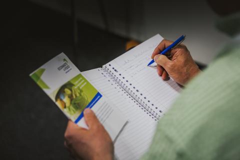 Person writing on a notebook holding a Interreg Europe brochure 