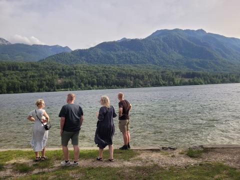 Four members of the Danish team stand by the lakeshore, looking out over the water towards the lush green mountains in Bohinj, Slovenia.