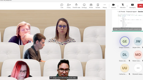 Screenshot of an online meeting using a virtual auditorium background, with participants' images placed in theater-style seats. The participants appear engaged in the project discussion, with financial report slides visible on the right side.