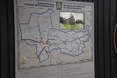 The photo shows a detailed map of Butrimonys and its surroundings, where places of interest are highlighted in both Lithuanian and English. The map is part of an interactive exhibition, with key points of interest marked (pressing a button highlights a specific location on the map), along with accompanying photos and descriptions of the sites. In the upper right corner, there is a photo of one of the places – the wooden Raižiai Mosque, a Tatar place of worship.