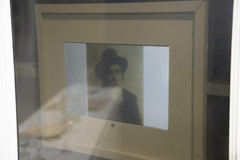 In the display case, a screen shows a rotating slideshow of photographs depicting Jewish residents who lived in the Butrimonys borough. The images change periodically, allowing visitors to see and learn about the individuals who were part of the community.