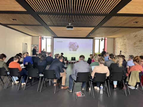 Audience seated at an event with a presentation screen displaying "ENAIBLER" and a speaker at the podium.