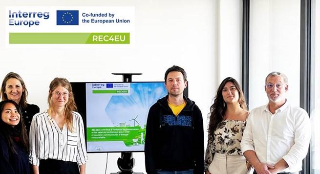 Group of people standing in front of a screen - logo REC4EU