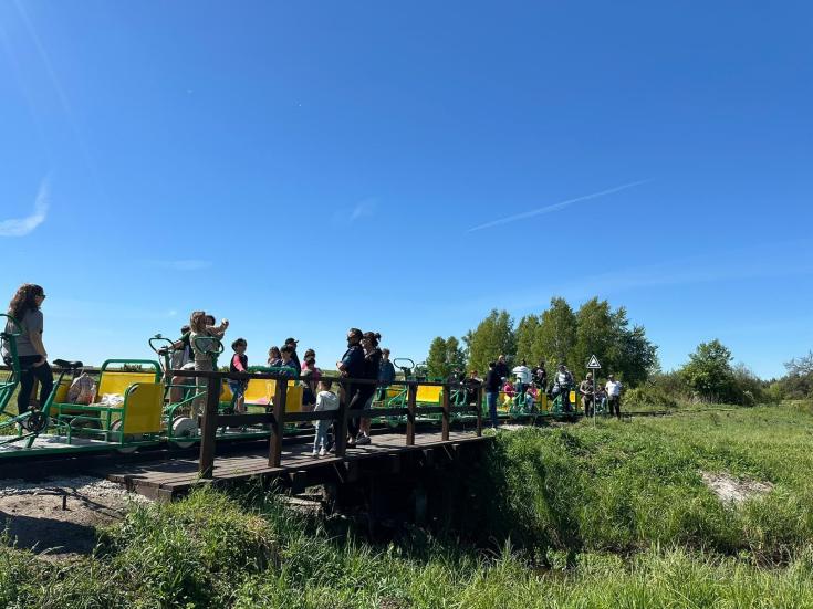 People on a green grassland going over a bridge above the river and the sky is blue.