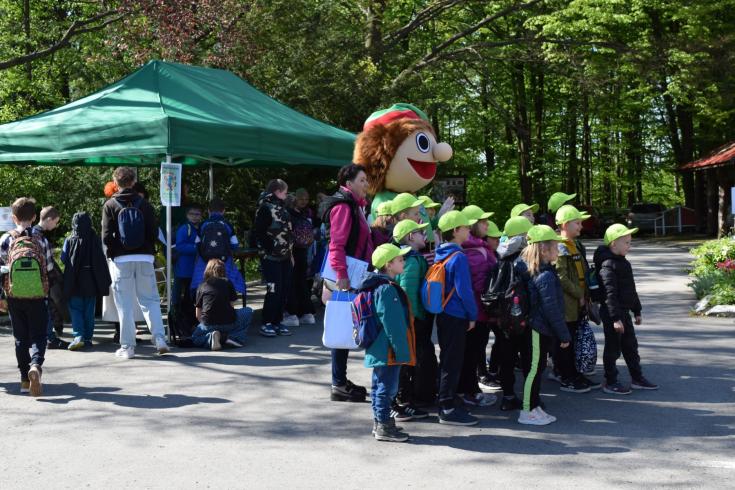 Group of children with green caps on their heads smiling at the camera with a mascot.