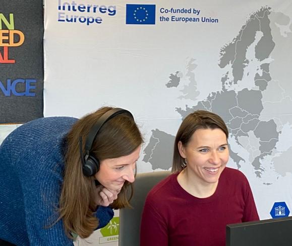 two people looking at a computer screen and web camera with a map of Europe and Interreg Europe logo on the background