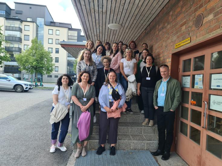 The group of INVOLVIM project participants poses in front of a typical Finnish red brick building housing the immigration office "Moni," where they had a study visit.