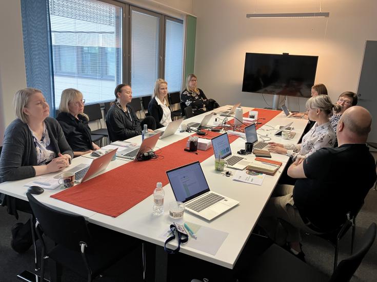 A group of people is sitting around a meeting table in a meeting room.