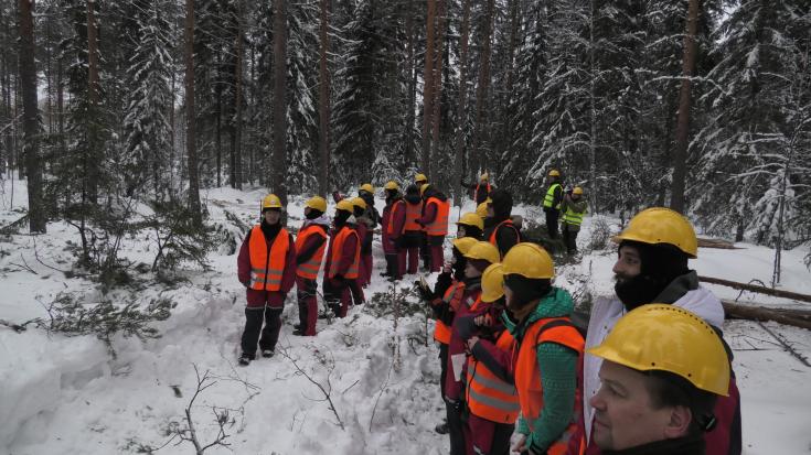 Big group of people in the snowy coniferous forest with red overalls and yellow helmets.