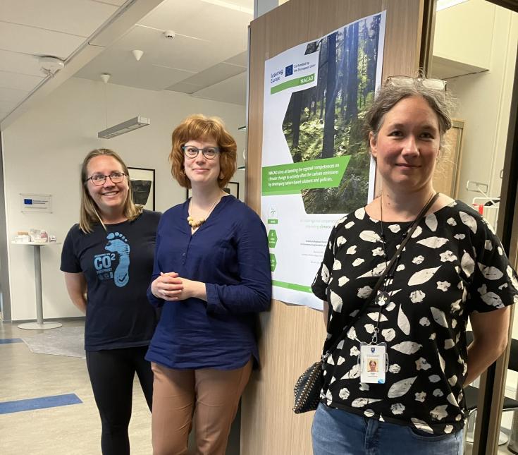 Three smiling women are standing and leaning against the meeting room wall.