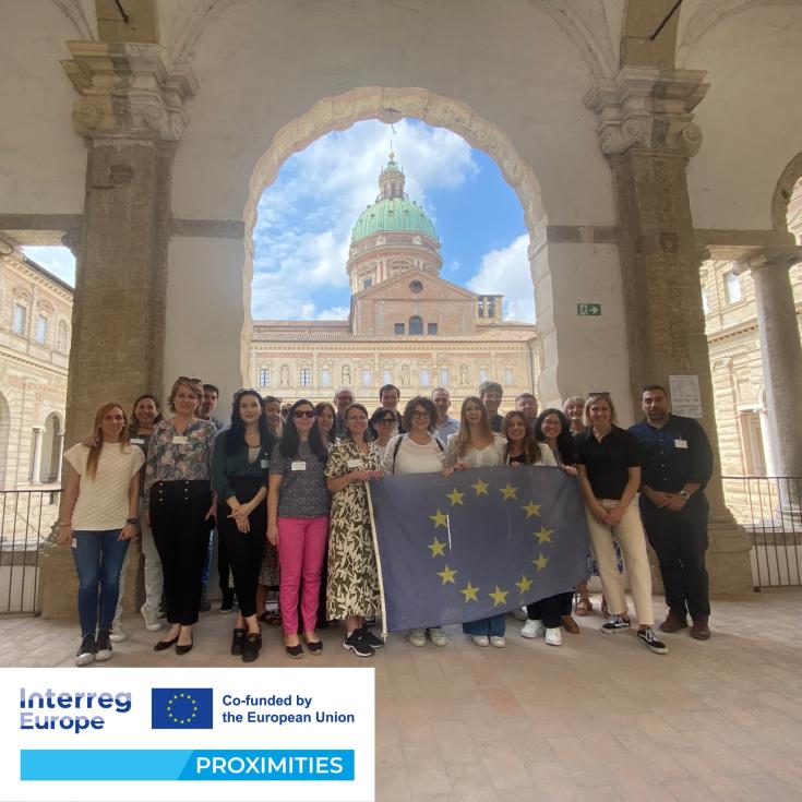 Group photo of PROXIMITIES partners standing holding EU flag with PROXIMITIES logo in corner