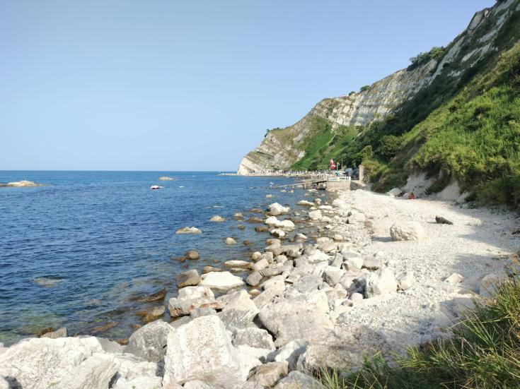 White, rocky seashore and steep slopes rising up from the blue sea.