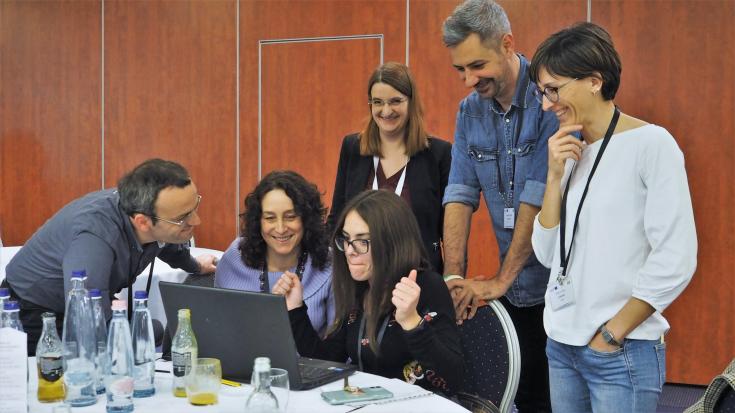 group of people gathered around a laptop and smiling