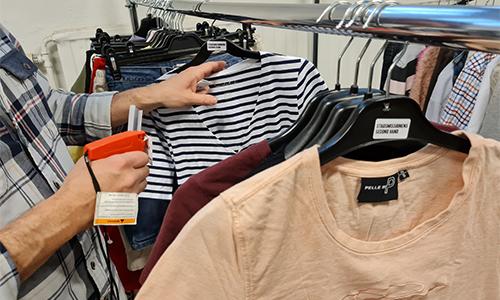 A person – only seen by hands – marking second-hand clothes on a hanger rack