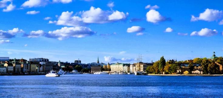 skyline of Stockholm pictured from the seaside with water, buildings, trees, blue sky and some clouds
