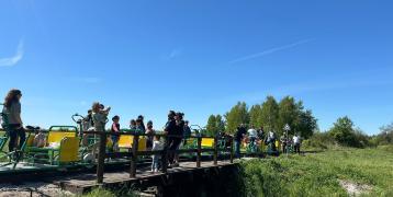 People on a green grassland going over a bridge above the river and the sky is blue.