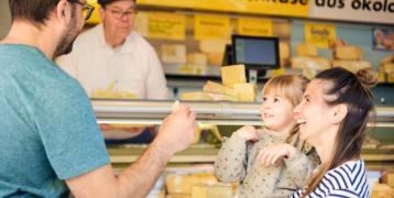 A family buys regional products from a cheese counter at a weekly market.