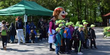 Group of children with green caps on their heads smiling at the camera with a mascot.