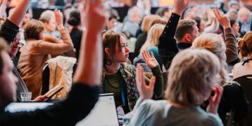 Group of people raise hands and look towards a stage at event