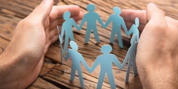 hands encircling and supporting paper people standing in a circle holding hands
