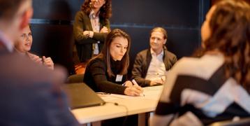 Person writing on paper with people standing around