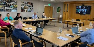 People sitting in a meeting room, a monitor displays online participants