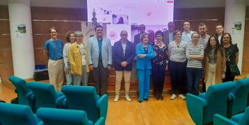 Group photo of participants from the GIFT regional stakeholder group meeting, standing in a conference room with teal auditorium chairs in the foreground. Behind them is a presentation screen displaying a virtual meeting interface. The group consists of men and women from various project partner organizations, dressed in business casual attire, gathered to discuss green infrastructure and biodiversity strategies.