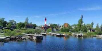 An island with a red and white lighthouse on the background, old piers in the front